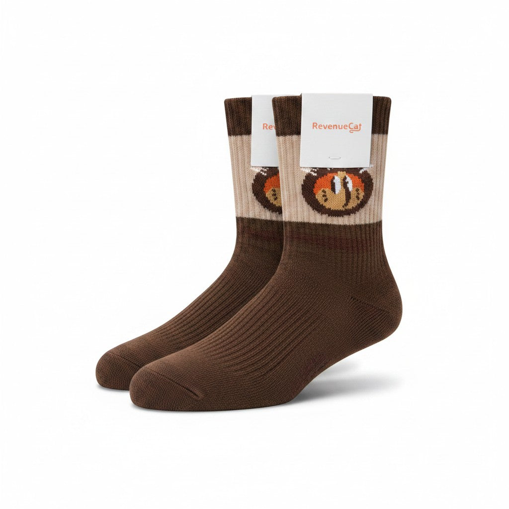 The RevenueCat Swag Store crew socks in chocolate brown and beige with a stylized cat face graphic on the ribbed cuff.