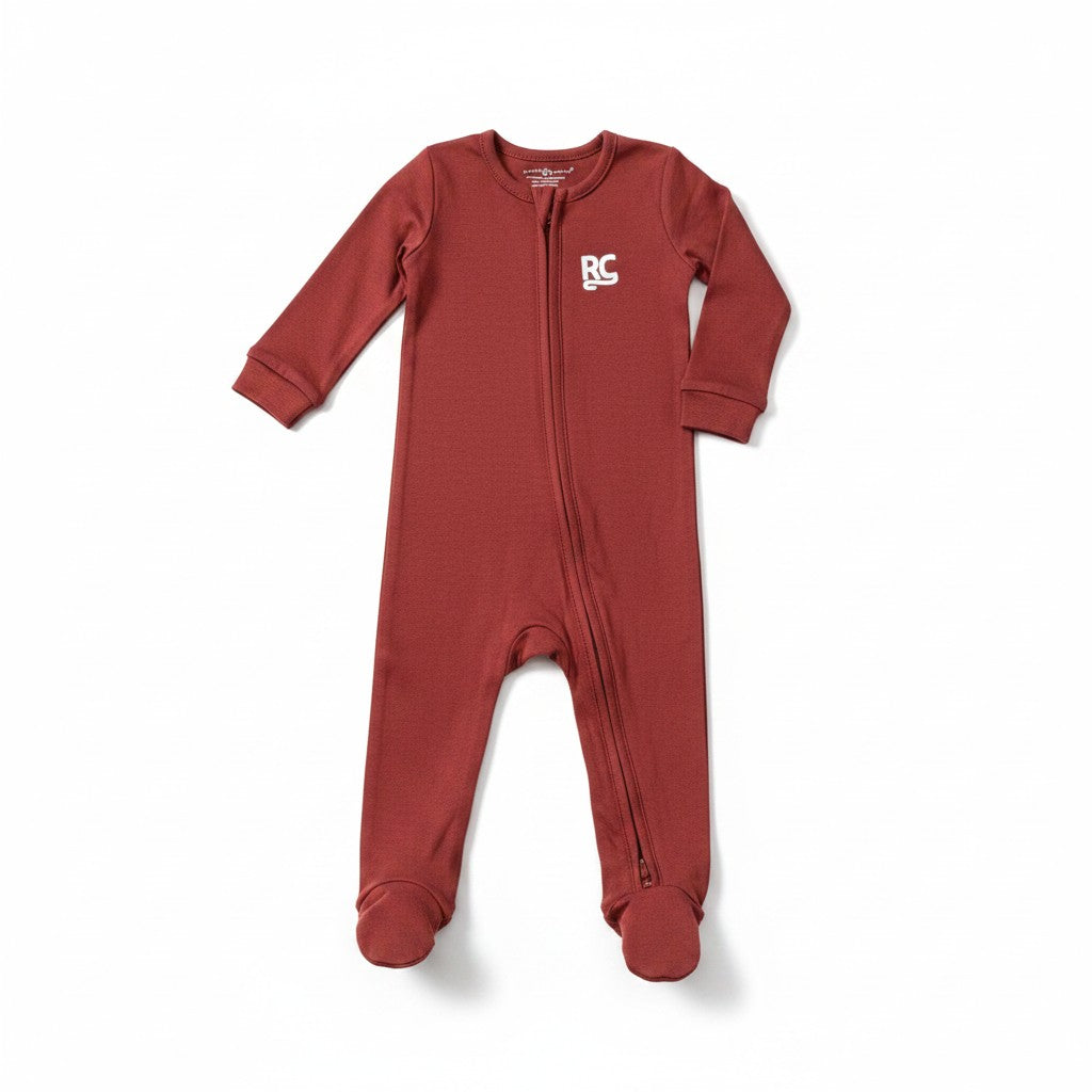 The RevenueCat Swag Store rust-red long-sleeve infant footed zipper romper with white RC logo on the chest.